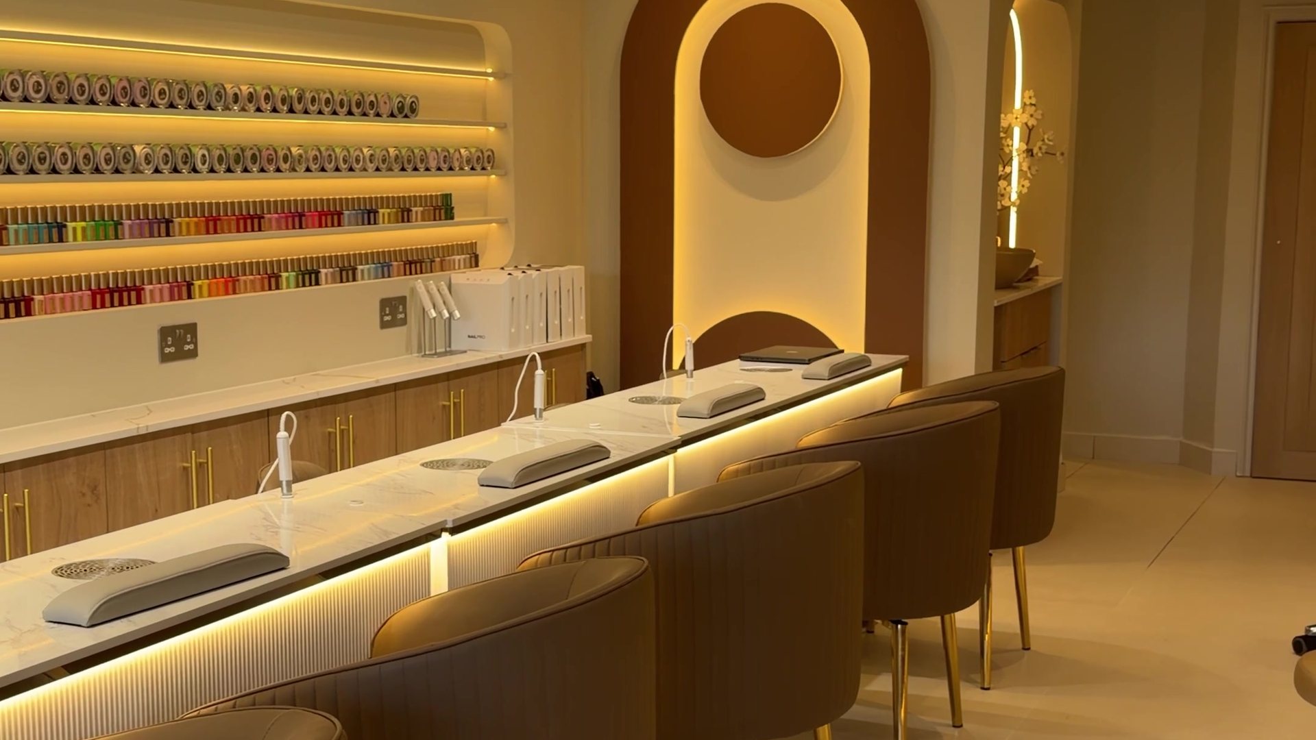 The nail bar at KINU Stoneleigh — lit shelves of colour along one wall, marble counter and a backlit arch at the end of the room