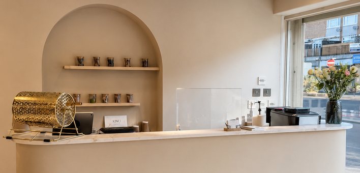 The curved reception desk at KINU Stoneleigh, with an arched shelf of tea behind and the window onto Stoneleigh Broadway to the right