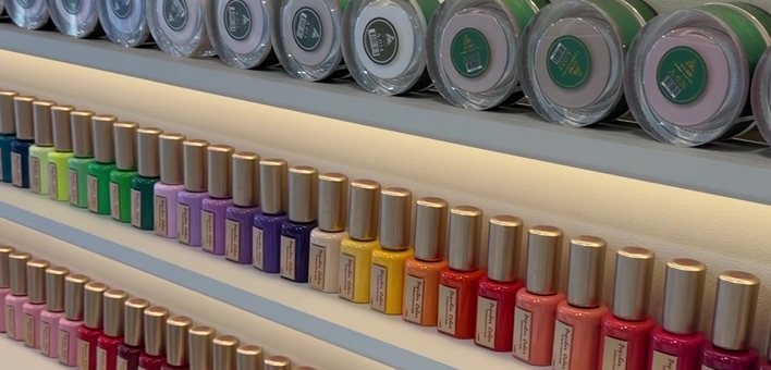 Rows of gel colours and dip powders on the lit shelves above the nail bar