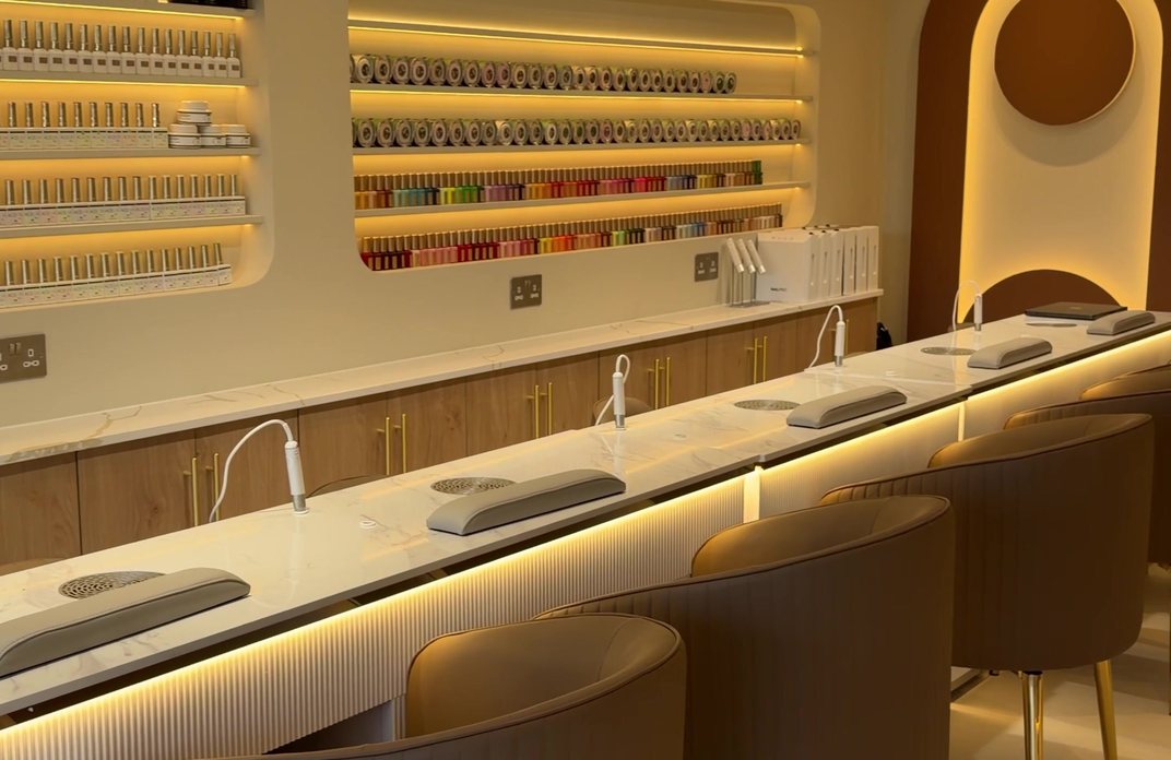The nail bar at KINU Stoneleigh — a marble counter running the length of the room beneath lit niches of colour, with a backlit arch at the far end