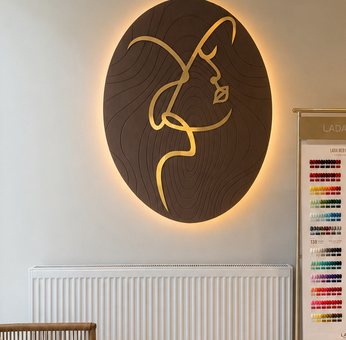 A backlit line drawing of a face, in gold on dark timber, on the wall above the waiting bench