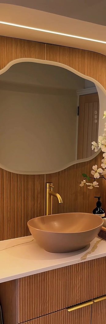 The head spa station — a curved mirror, brushed gold tap and stone basin set into fluted timber